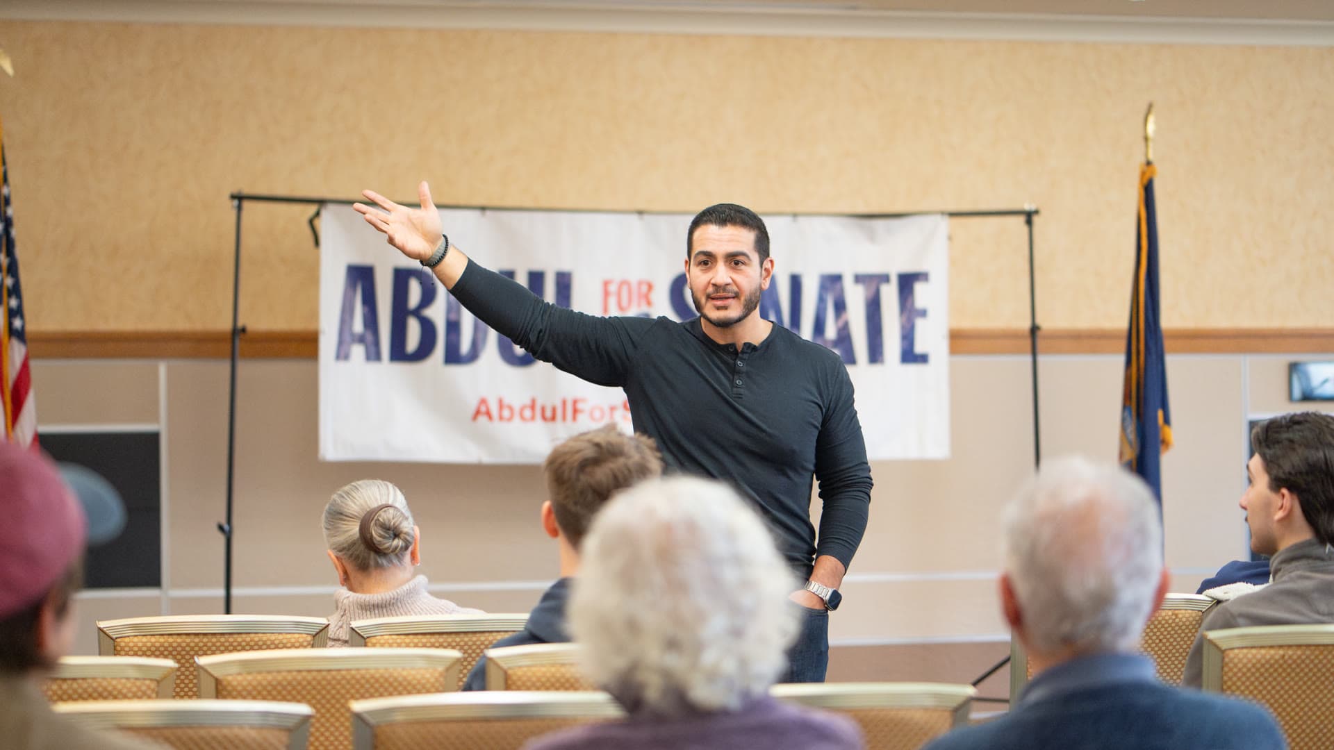 Abdul El-Sayed speaking to a small seated audience in a meeting room, one arm raised.
