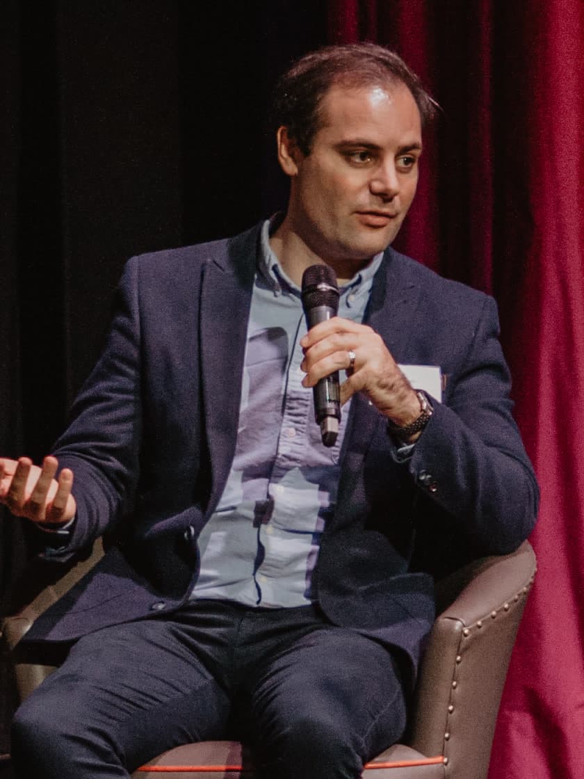 Ben Delo speaking into a microphone on a conference stage