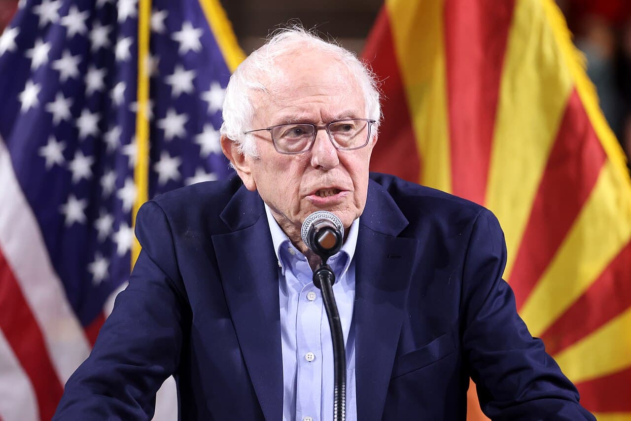 Bernie Sanders speaking into a microphone with U.S. and Arizona flags behind him.