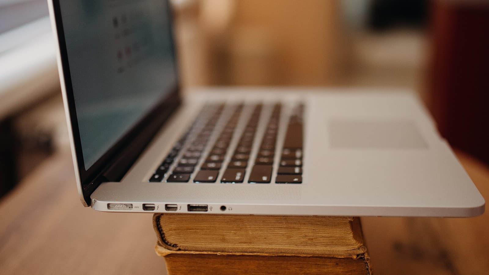 A laptop resting on a stack of books on a wooden table.
