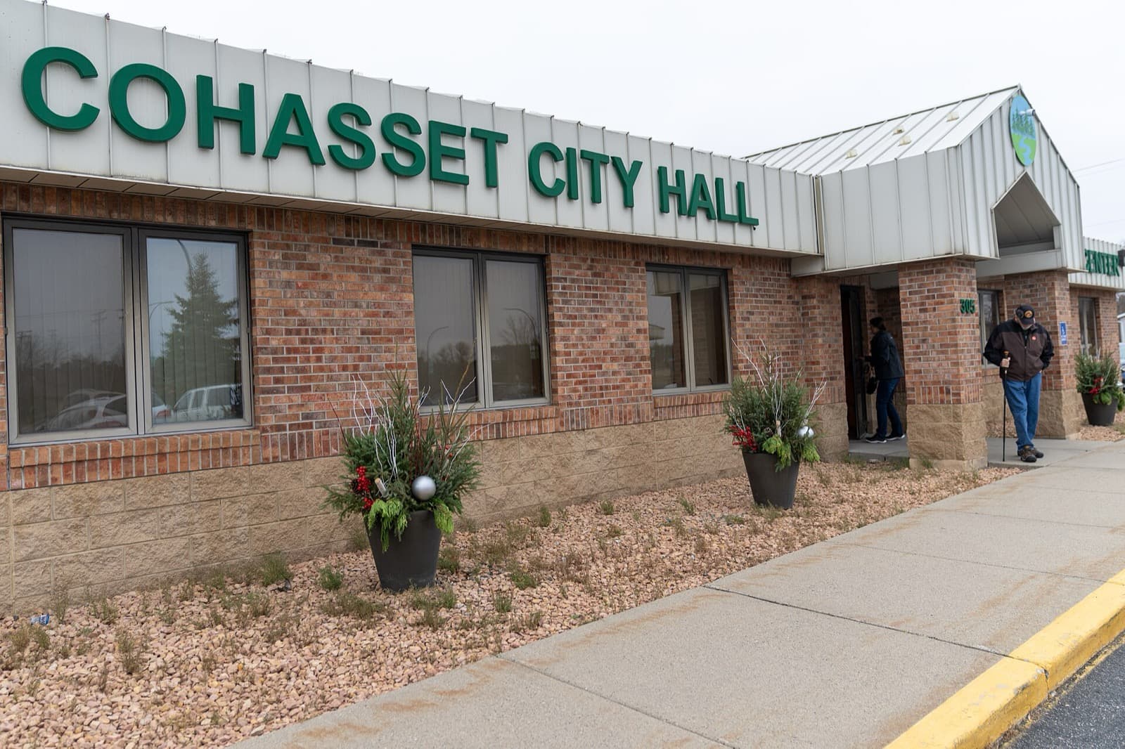 A voter with a cane walks out of Cohasset City Hall, a brick building with large green lettering, on Election Day.