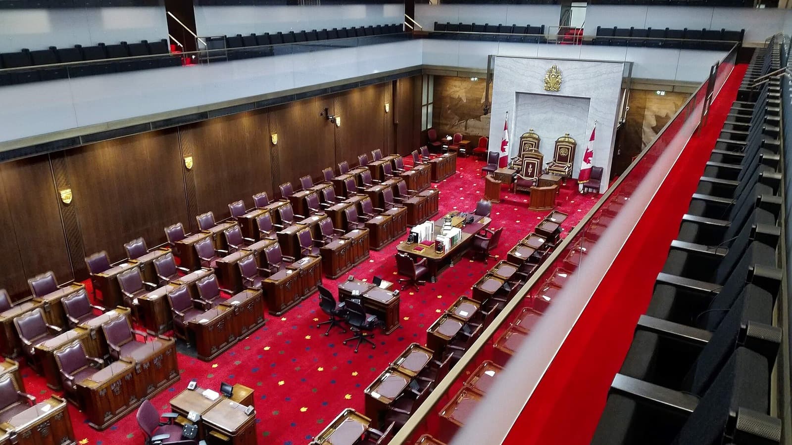 The chamber in the Senate of Canada Building in Ottawa, with red carpet, desks and the speaker's chairs.