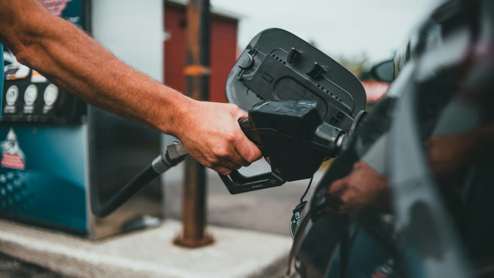 A hand holds a fuel nozzle while refueling a car.