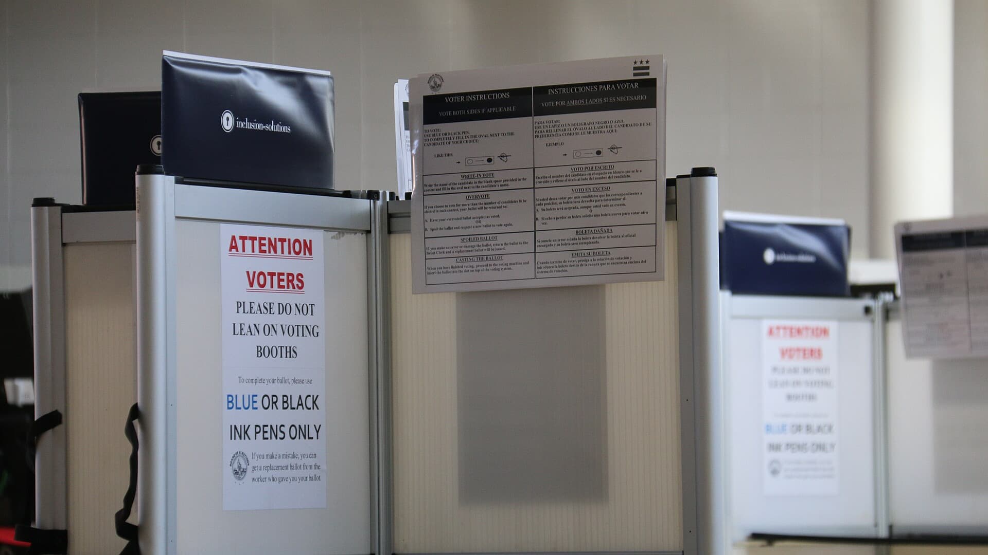 Voting booths at a Washington, D.C., polling station with "Attention voters" signs asking voters to use blue or black ink, and bilingual ballot instructions posted above.