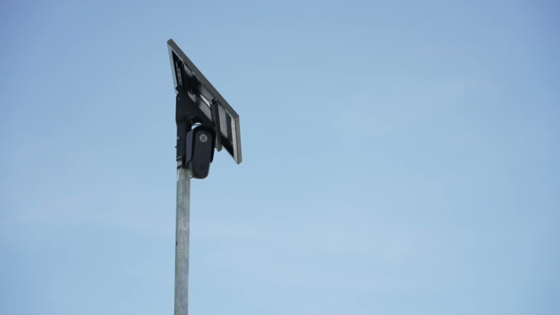 A pole-mounted automated license-plate reader and solar panel against a blue sky.