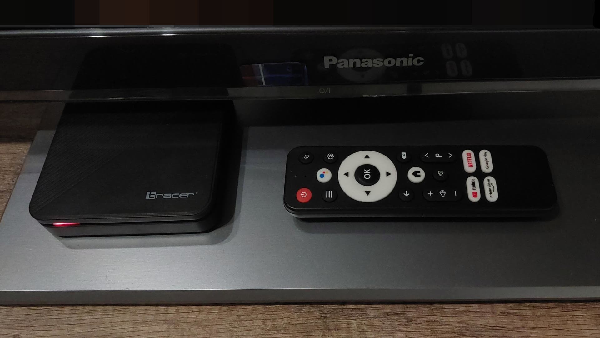 An Android TV set-top box and its remote control on a shelf below a television