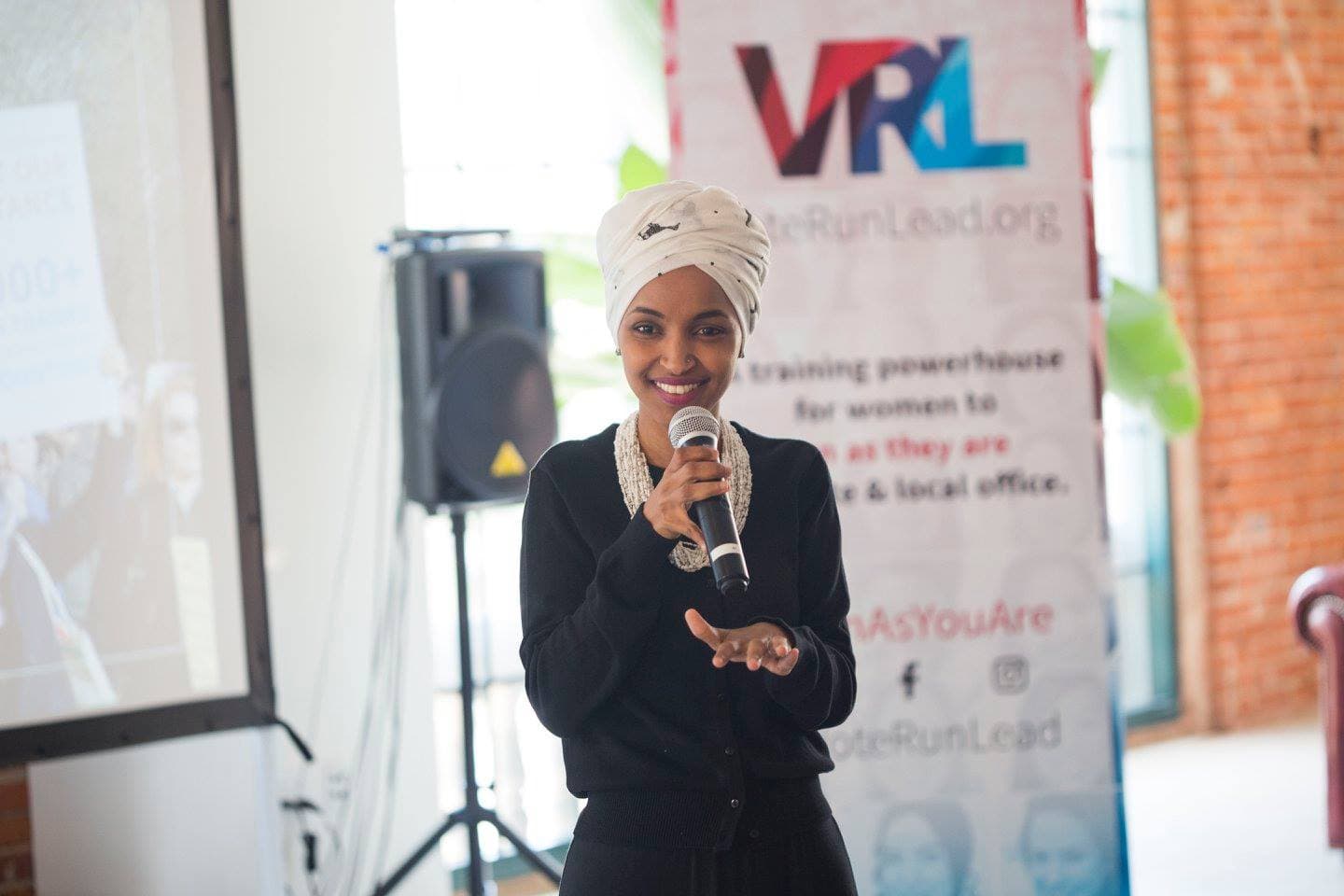 Ilhan Omar speaking into a microphone at a 2018 VoteRunLead event.
