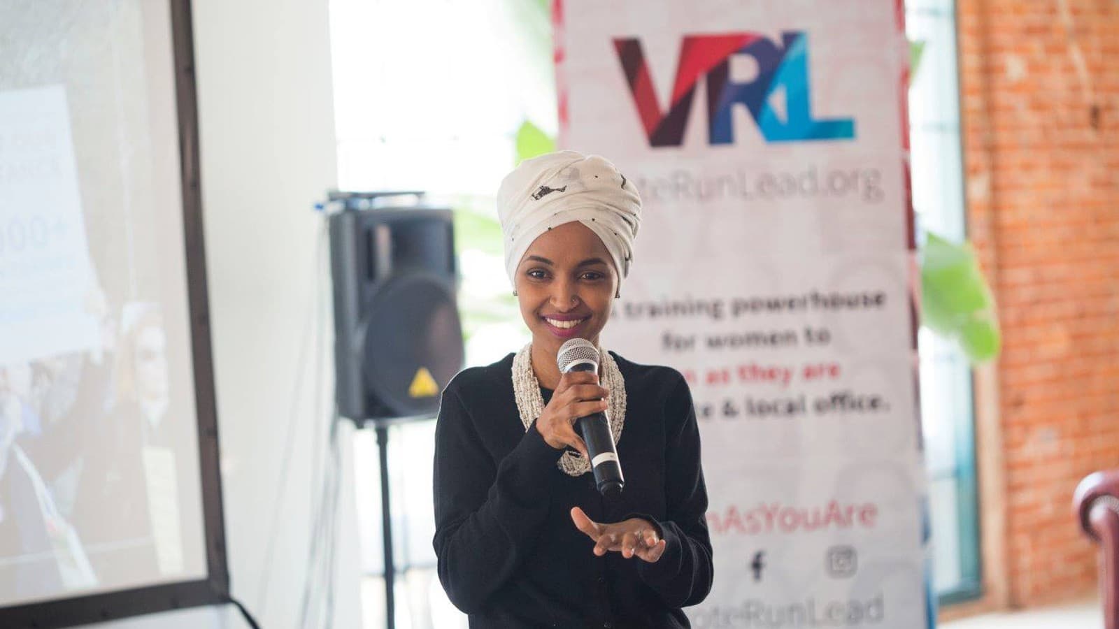 Ilhan Omar holding a microphone at a VoteRunLead event in 2018.