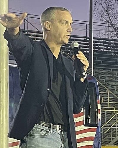 Corey Lewandowski speaking into a microphone at an outdoor rally