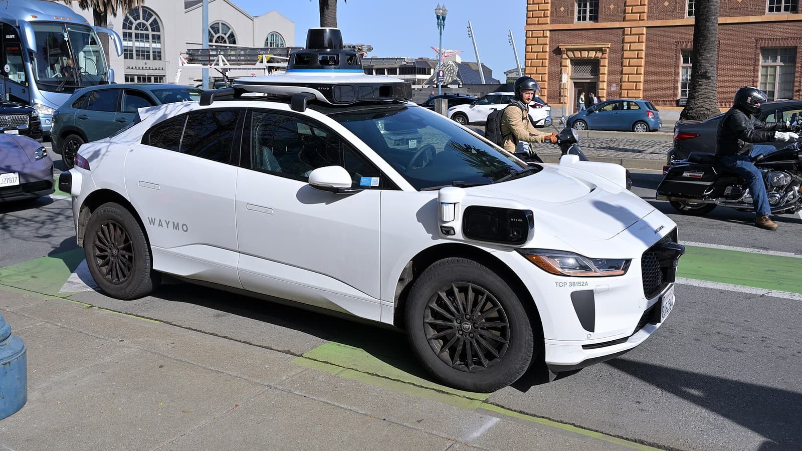A white Waymo autonomous taxi with roof-mounted sensors on a San Francisco street.