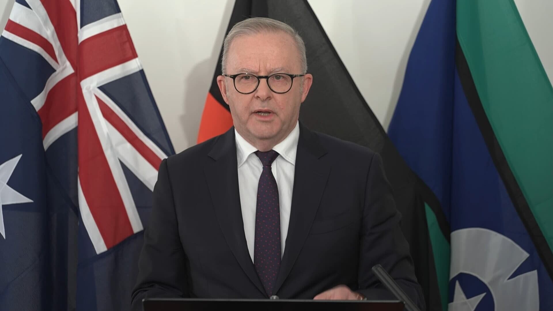 Australian Prime Minister Anthony Albanese speaks at a press conference with Australian and Indigenous flags behind him.