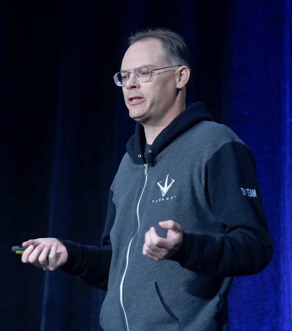 Tim Sweeney, wearing glasses and a gray zip-up hoodie, speaks on a stage