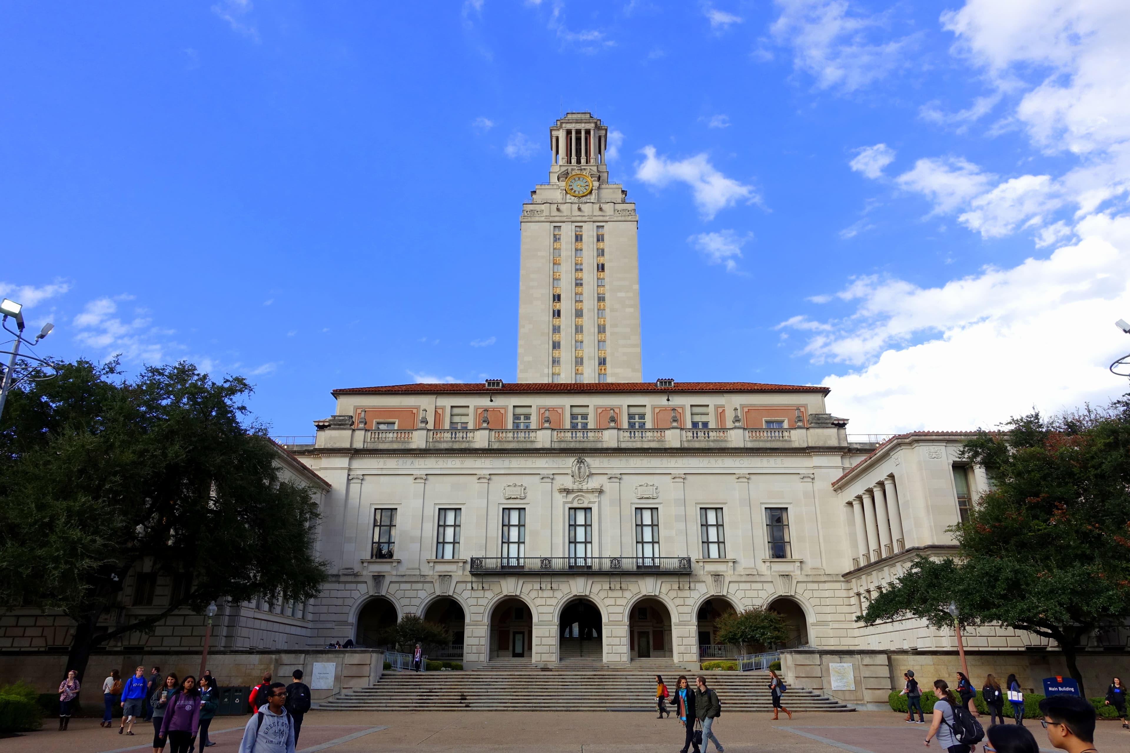 The UT Austin Main Building and Tower, with students walking across the front plaza.