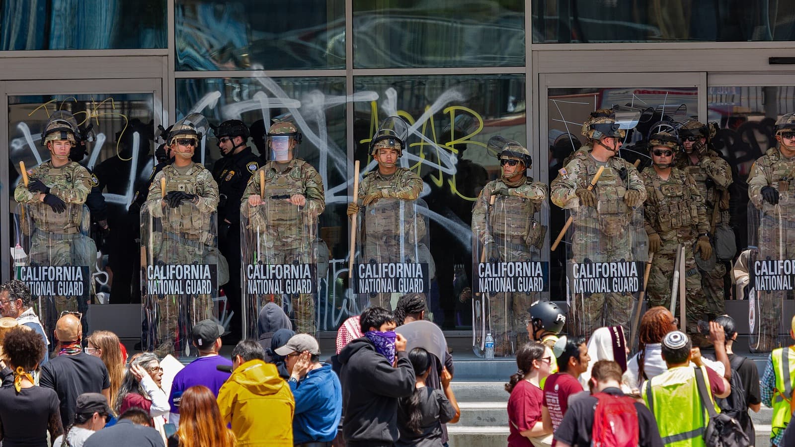 California National Guard troops stand behind shields as people gather in Los Angeles.
