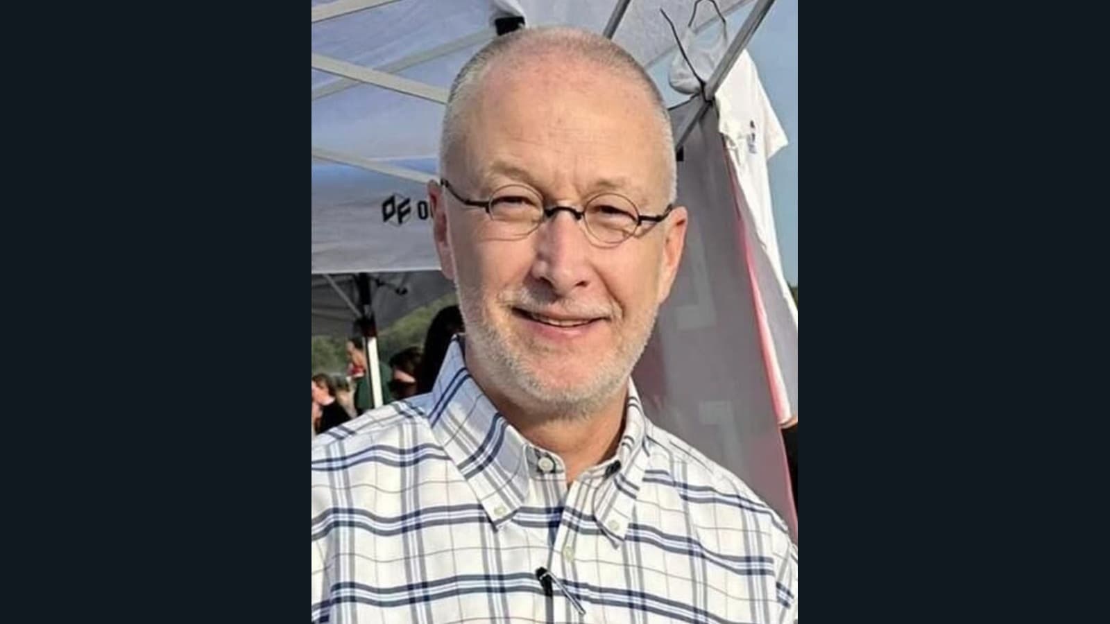 Brent Taylor wearing glasses and a checked shirt beneath an outdoor canopy.