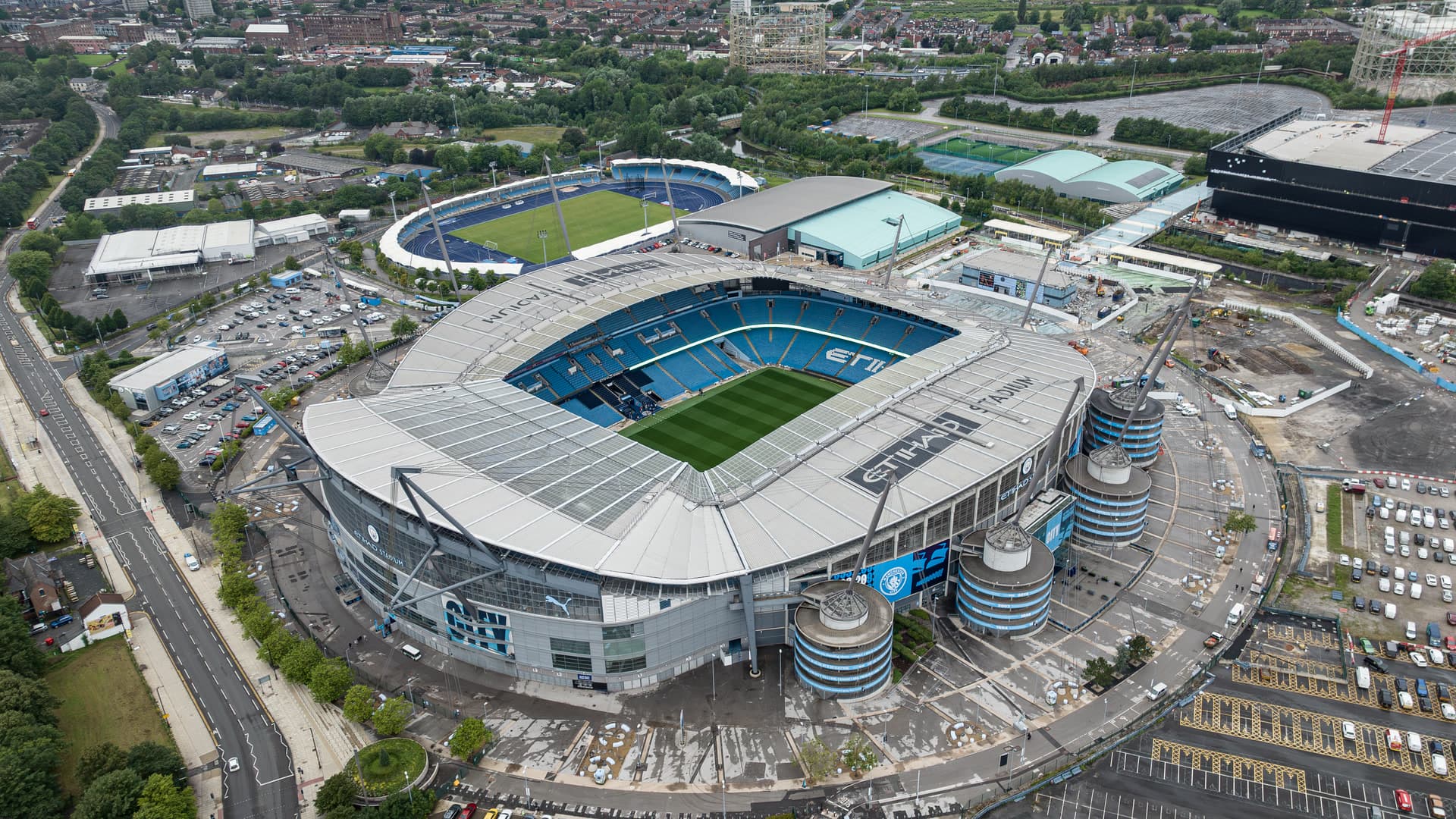Aerial view of the Etihad Stadium in Manchester, home of Manchester City, with the pitch, the surrounding car parks and the neighboring campus buildings.